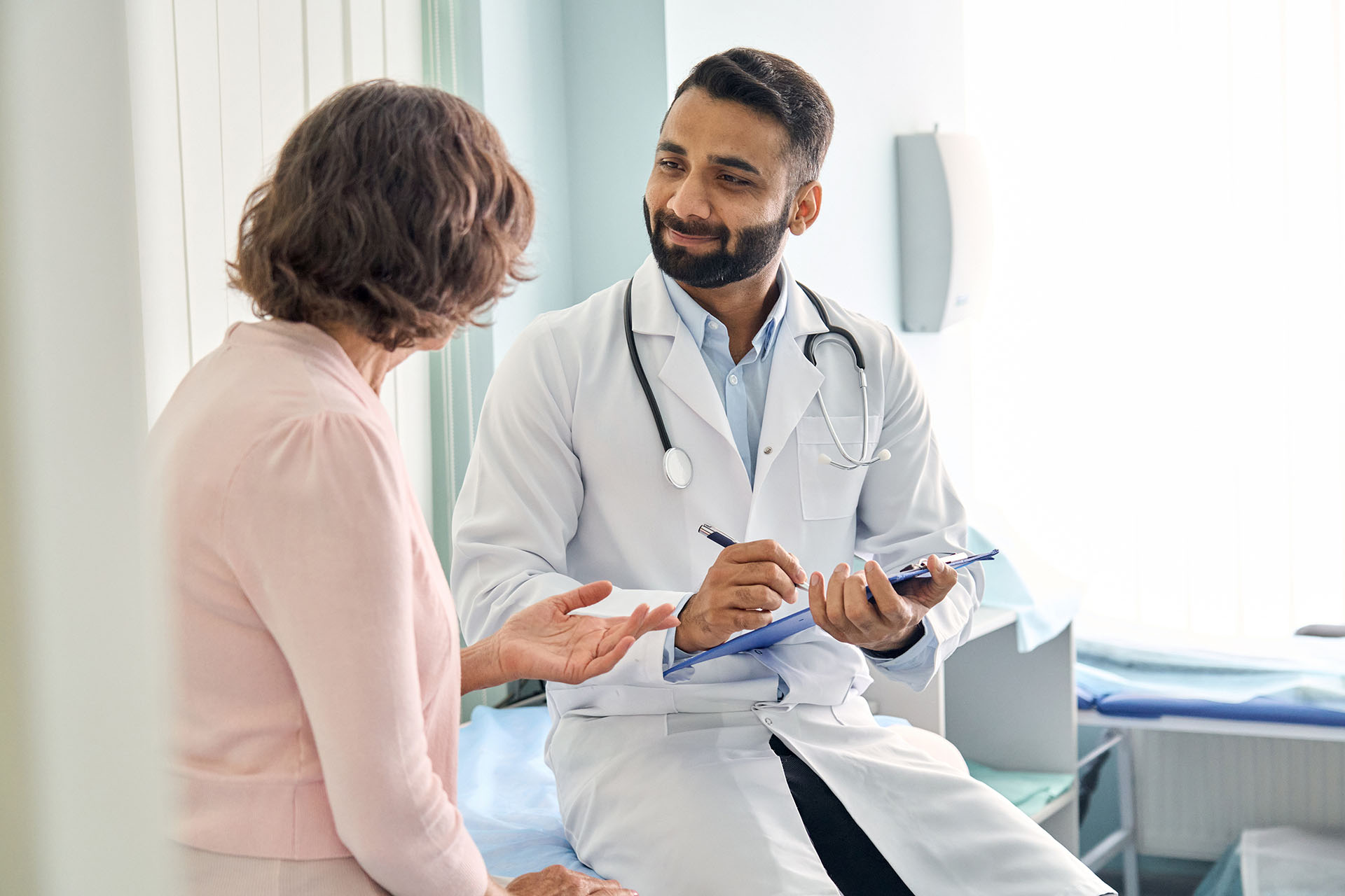 Indian male doctor consulting senior patient filling medical form.